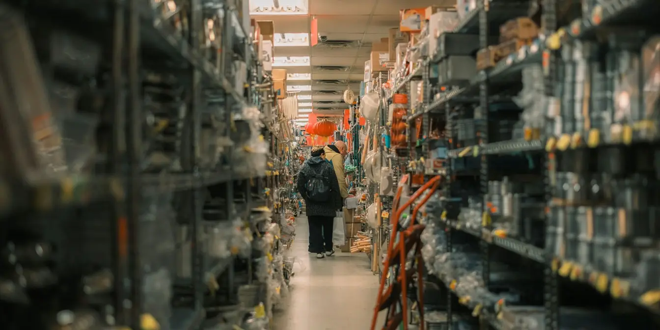 Two shoppers at the far end of a long, crowded hardware store aisle