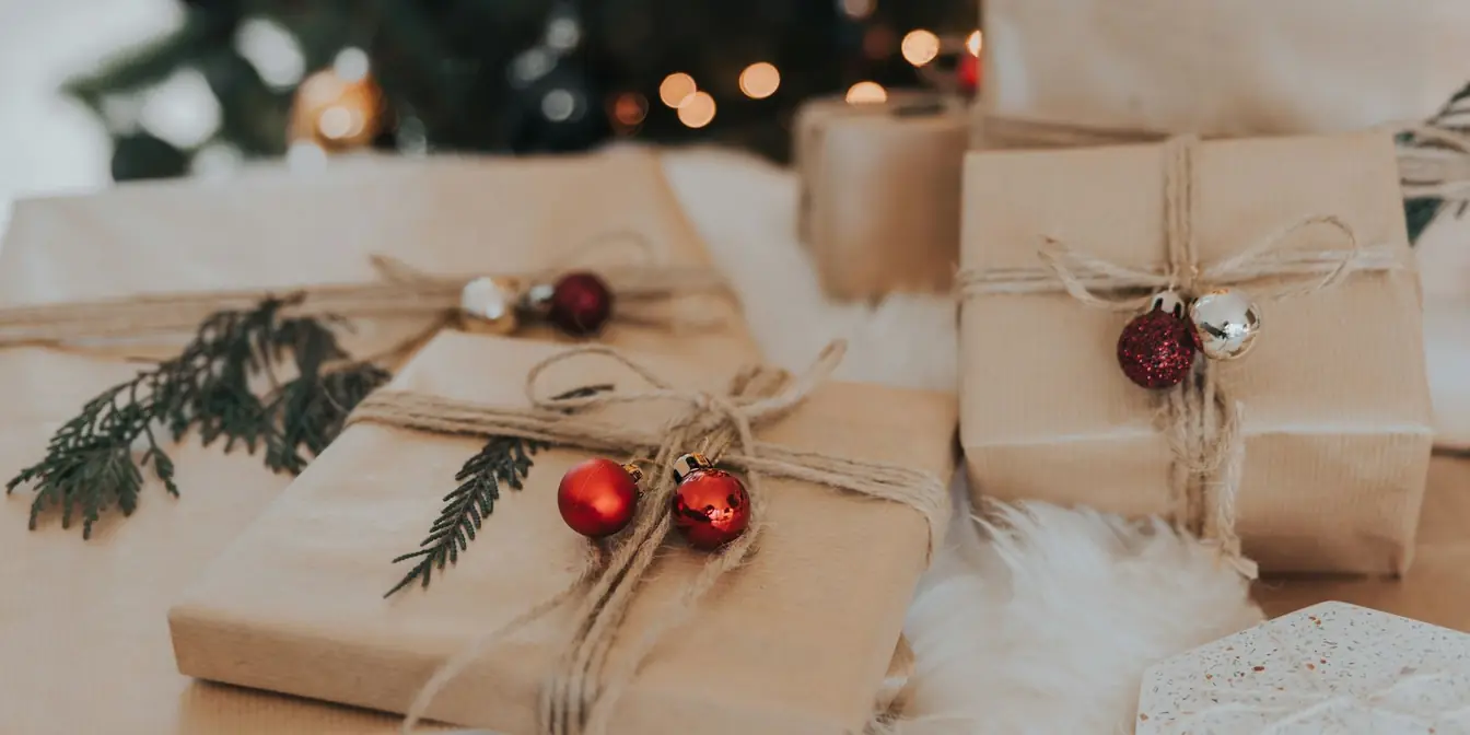Presents wrapped in brown paper and twine with small red baubles, fairy lights behind